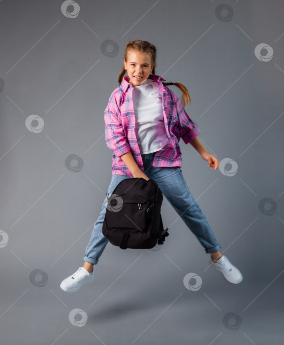 Скачать школьница с рбкзаком прыгает на сером фоне. школьный контент фотосток Ozero