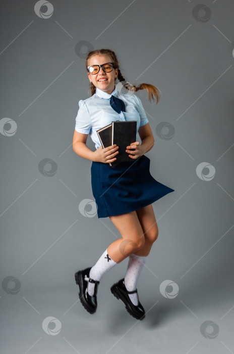 Скачать Счастливая школьница, стоящая с книгой в руках, изолированная на сером фоне фотосток Ozero