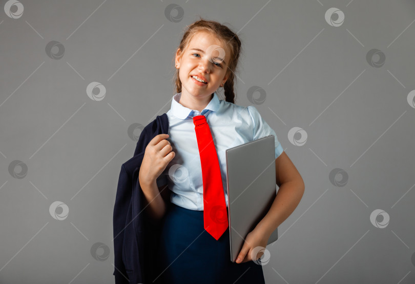 Скачать Счастливая улыбающаяся школьница 12 лет, держащая в руках ноутбук, выделенная на сером фоне, смотрит в камеру. фотосток Ozero
