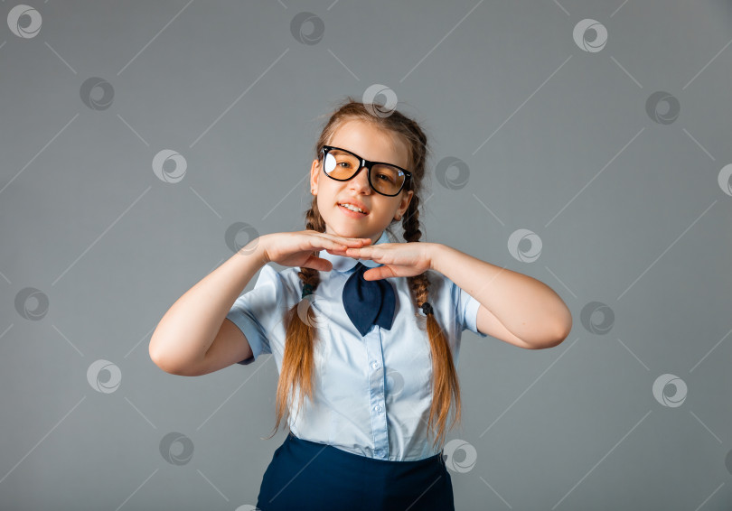 Скачать Возбужденная маленькая девочка в школьной форме и очках веселится и показывает десять пальцев, стоя на сером фоне фотосток Ozero