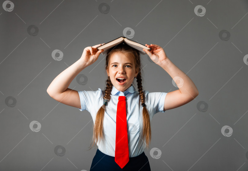 Скачать Девочка 12 лет в школьной форме с книгой над головой, выделенная на сером фоне фотосток Ozero