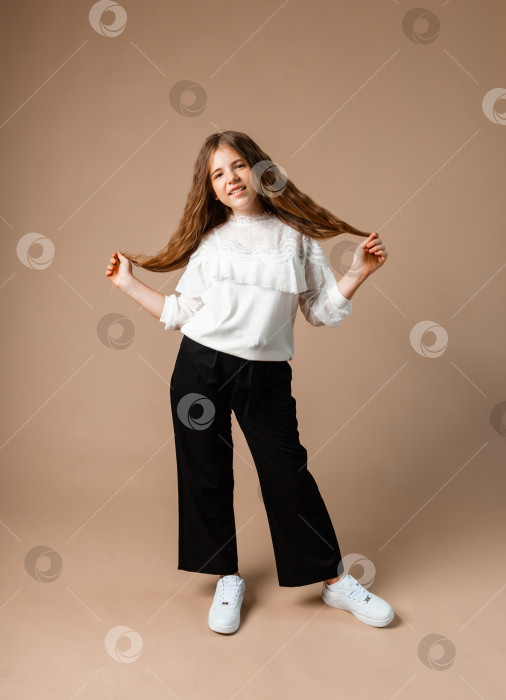 Скачать Портрет счастливой маленькой девочки 12 лет, стоящей и позирующей на фоне студии фотосток Ozero