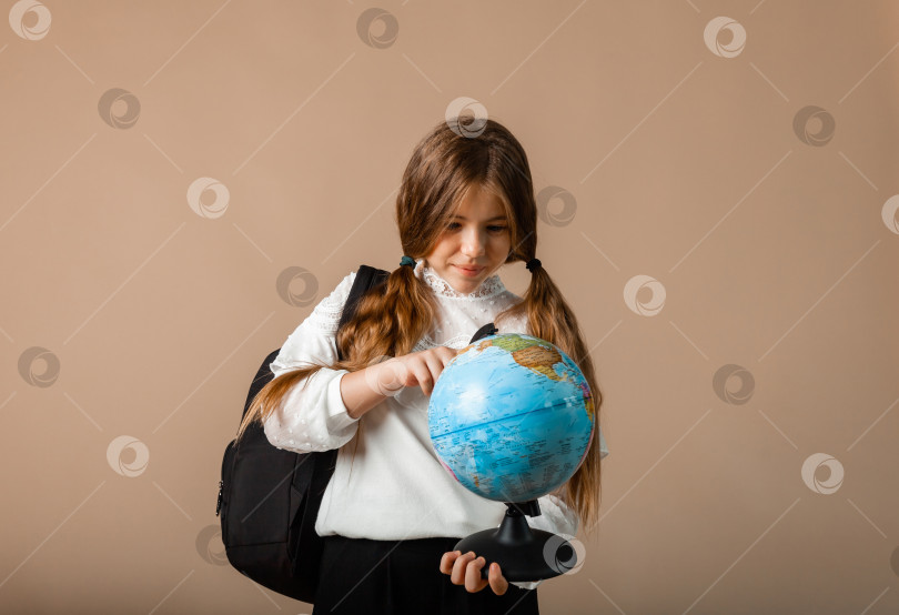 Скачать школьница держит глобус, показывая пальцем пустое пространство, изолированное на фоне студии фотосток Ozero