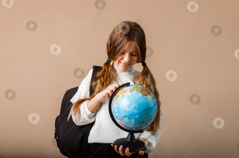 Скачать школьница держит глобус, показывая пальцем пустое пространство, изолированное на фоне студии фотосток Ozero