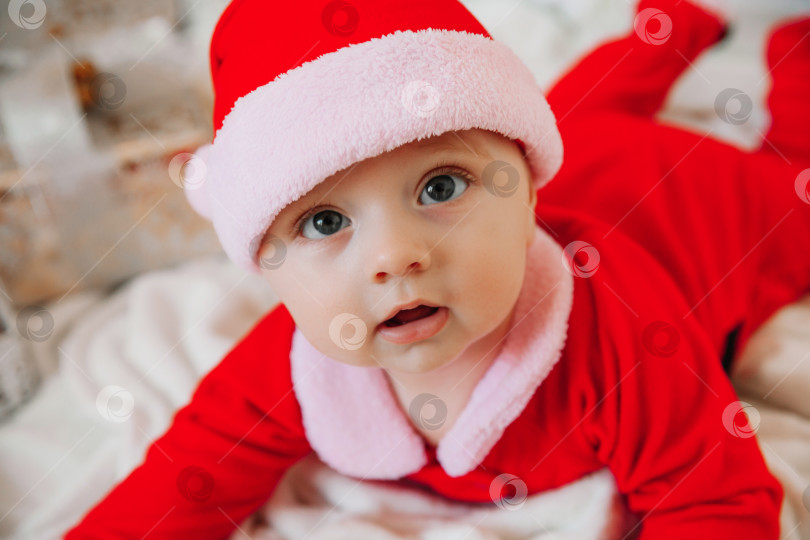 Скачать милый малыш 6 месяцев от роду в костюме Санты лежит на одеяле возле рождественской елки. Рождество 2022 года фотосток Ozero