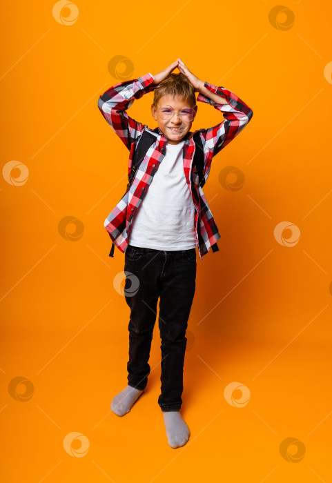 Скачать Симпатичный школьник в клетчатой рубашке обхватывает голову руками. изоляция на желтом фоне. фотосток Ozero