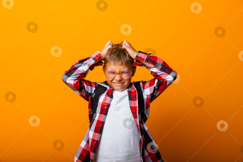 Скачать Симпатичный школьник в клетчатой рубашке обхватывает голову руками. изоляция на желтом фоне. фотосток Ozero