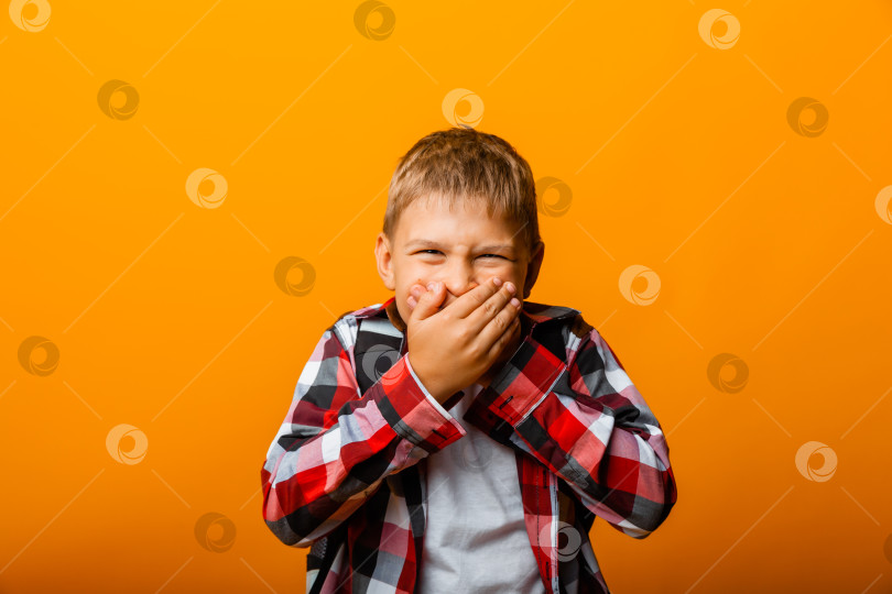 Скачать шокированный маленький мальчик в красной рубашке, прикрывающий рот руками на желтом фоне фотосток Ozero