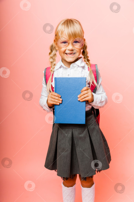 Скачать Портрет милой маленькой девочки на розовом фоне. Ребенок-школьница смотрит в камеру, держит в руках книгу и поправляет очки. Концепция образования. Пространство для копирования. фотосток Ozero