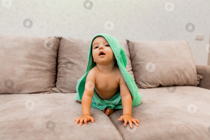 Скачать Симпатичный малыш, завернутый в полотенце, сидит на кровати. ребенок в банном полотенце. фотосток Ozero