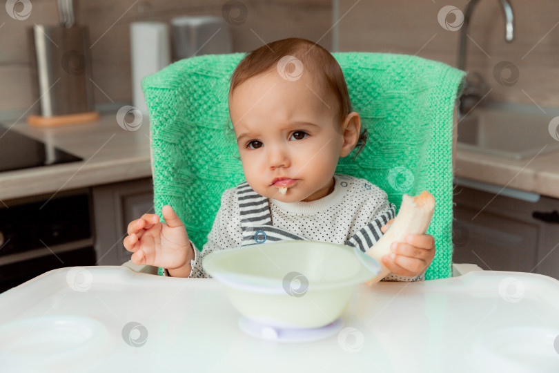 Скачать малыш сидит на высоком стульчике на кухне и ест банан. фотосток Ozero
