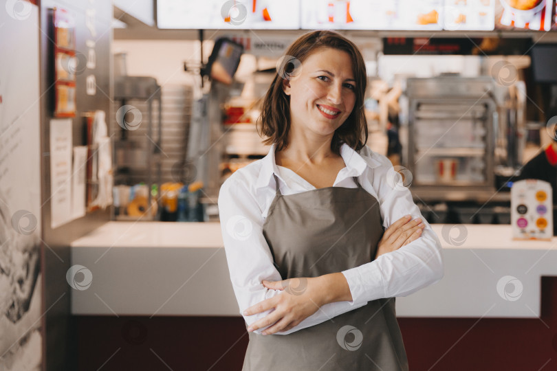 Скачать Молодая улыбающаяся женщина-бизнесвумен в фартуке стоит в кафе фотосток Ozero