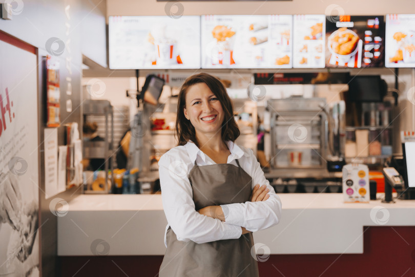 Скачать Молодая улыбающаяся женщина-бизнесвумен в фартуке стоит в кафе фотосток Ozero