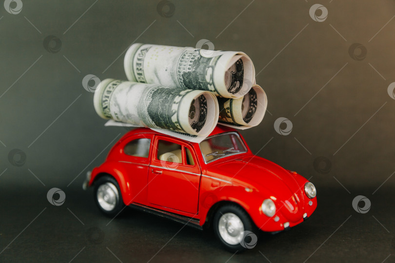 Скачать доллары, свернутые в трубочку на крыше миниатюрной модели автомобиля. красная машина с деньгами фотосток Ozero