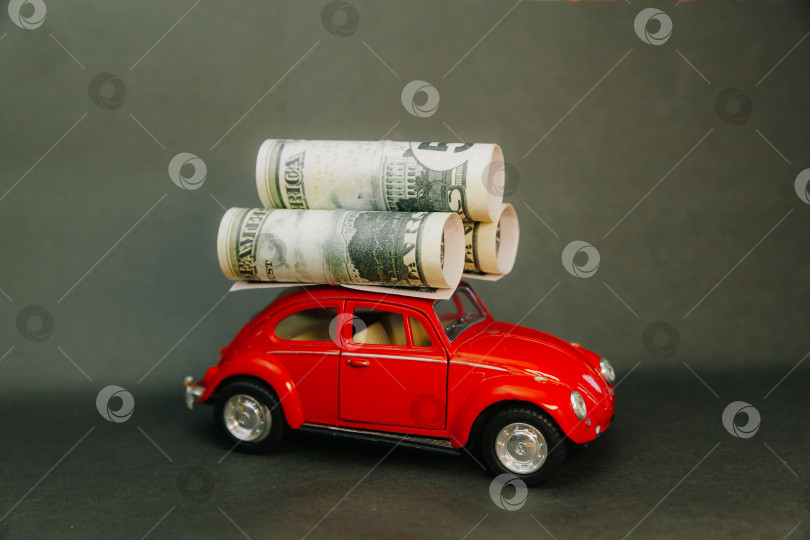 Скачать доллары, свернутые в трубочку на крыше миниатюрной модели автомобиля. красная машина с деньгами фотосток Ozero