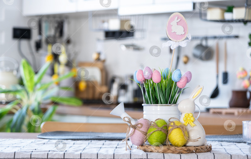 Скачать Пасхальное украшение из разноцветных яиц в корзинке и кролика на кухонном столе в деревенском стиле. Праздничный интерьер загородного дома фотосток Ozero