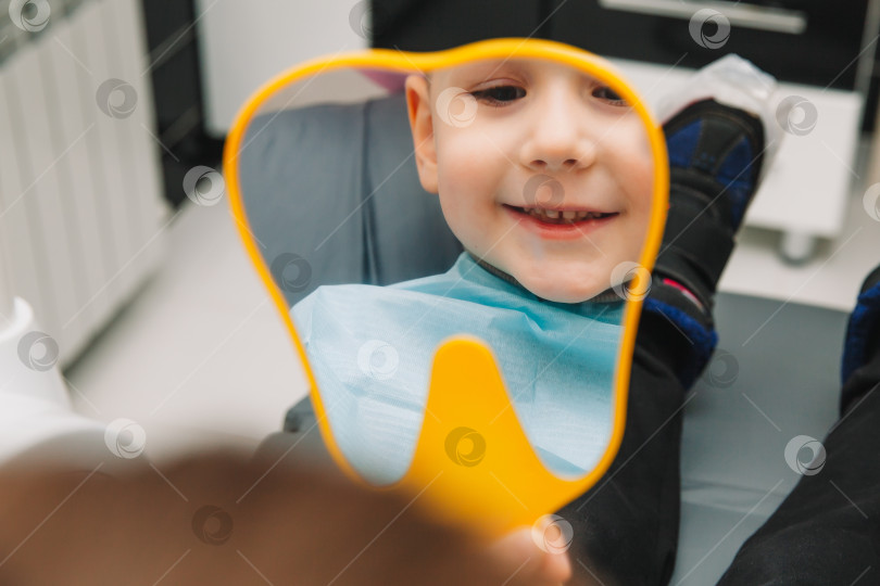 Скачать мальчик смотрится в зеркало с зубастой улыбкой, сидя на стуле рядом со стоматологом в стоматологическом кабинете. фотосток Ozero
