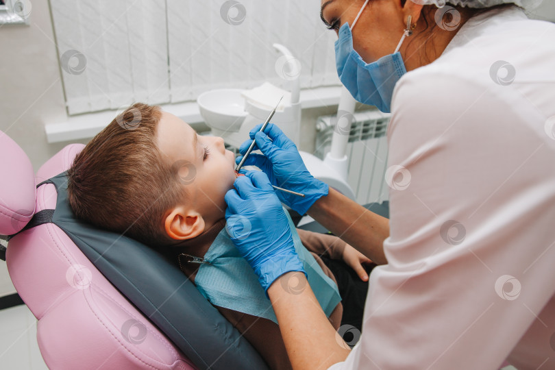 Скачать Детский стоматолог лечит детский кариес и ротовую полость мальчика, сидящего в стоматологическом кресле, во время регулярного медицинского осмотра фотосток Ozero