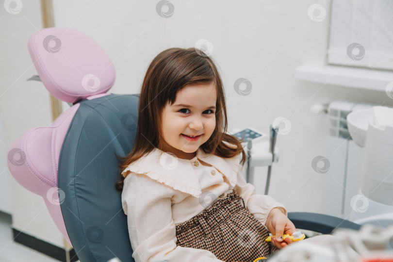 Скачать Портрет маленькой девочки, смотрящей в зеркало сбоку в детской стоматологии после стоматологической операции. фотосток Ozero