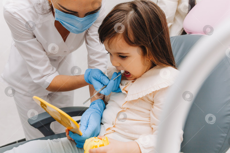 Скачать Портрет маленькой девочки, смотрящей в зеркало сбоку в детской стоматологии после стоматологической операции. фотосток Ozero