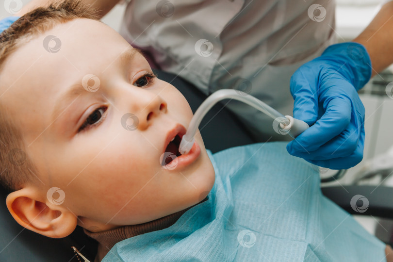 Скачать Детский стоматолог лечит детский кариес и ротовую полость мальчика, сидящего в стоматологическом кресле, во время регулярного медицинского осмотра фотосток Ozero