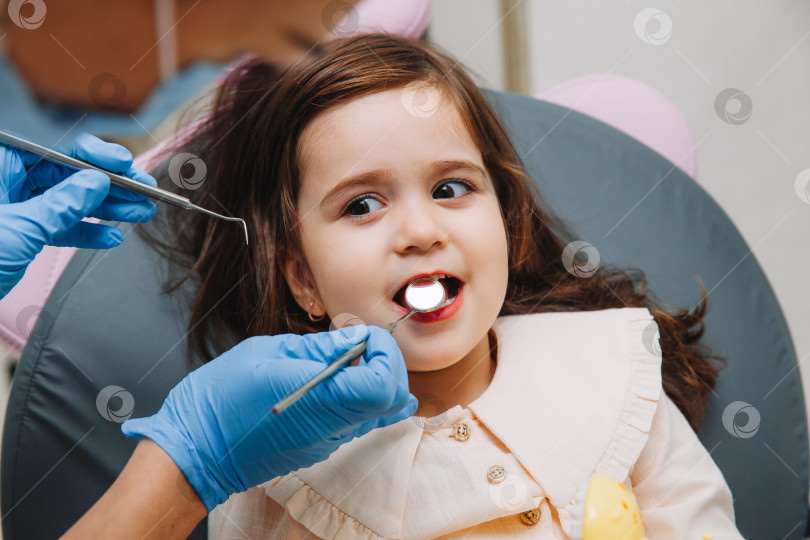 Скачать стоматолог, врач осматривает ротовую полость маленькой девочки, использует ротовое зеркало, молочные зубы крупным планом, концепция детской стоматологии, лечение зубов. фотосток Ozero