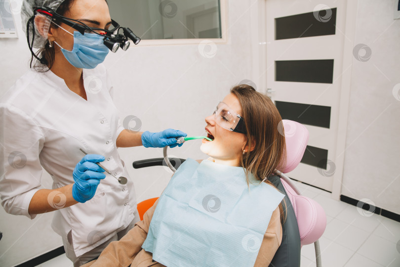 Скачать Женщина-стоматолог лечит зубы молодой женщины, лежащей в клинике. врач лечит зубы. фотосток Ozero