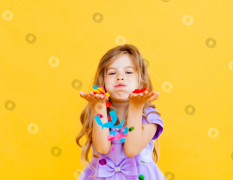 Скачать счастливая маленькая девочка со светлыми волосами и в голубом платье ловит конфетти на желтом фоне, концепция праздника фотосток Ozero