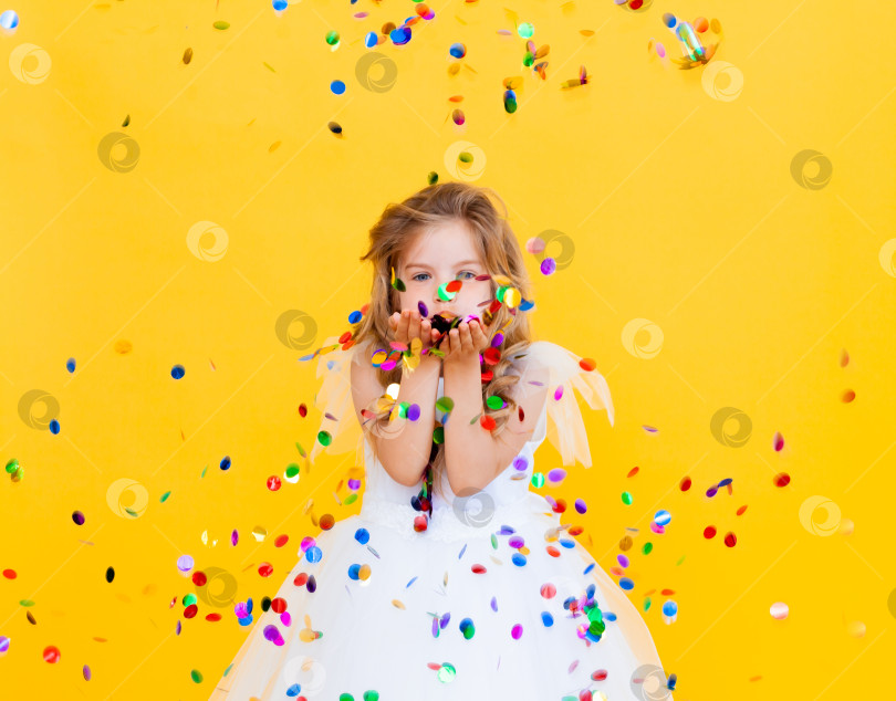 Скачать счастливая маленькая девочка со светлыми волосами и в белом платье ловит конфетти на желтом фоне, концепция праздника фотосток Ozero
