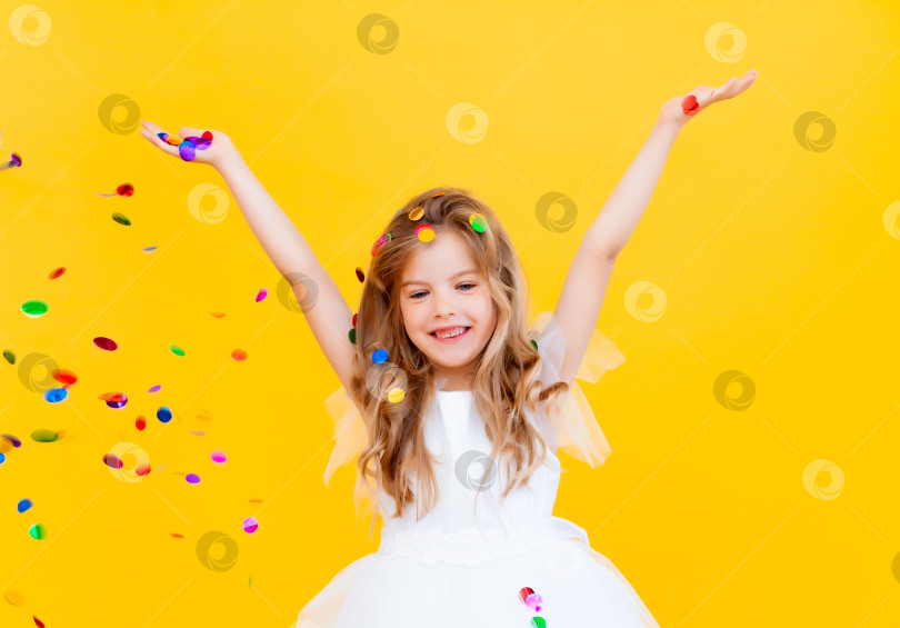 Скачать счастливая маленькая девочка со светлыми волосами и в белом платье ловит конфетти на желтом фоне, концепция праздника фотосток Ozero