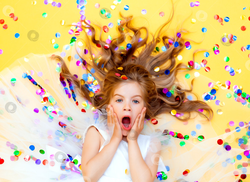 Скачать Счастливая маленькая девочка в белом платье празднует вечеринку с конфетти, вид сверху. День рождения ребенка, положительные эмоции. фотосток Ozero