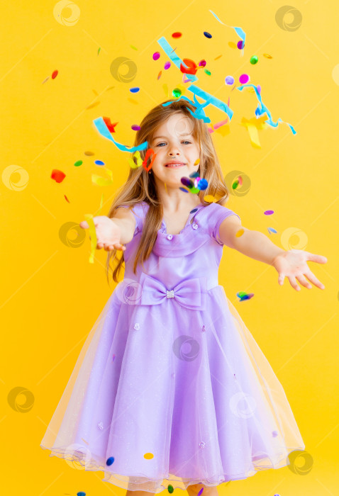Скачать счастливая маленькая девочка со светлыми волосами и в голубом платье ловит конфетти на желтом фоне, концепция праздника фотосток Ozero