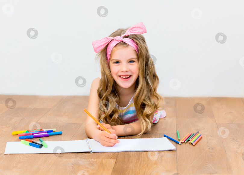 Скачать Маленькая девочка, лежа на полу, рисует карандашами. Симпатичная девушка рисует карандашами. фотосток Ozero
