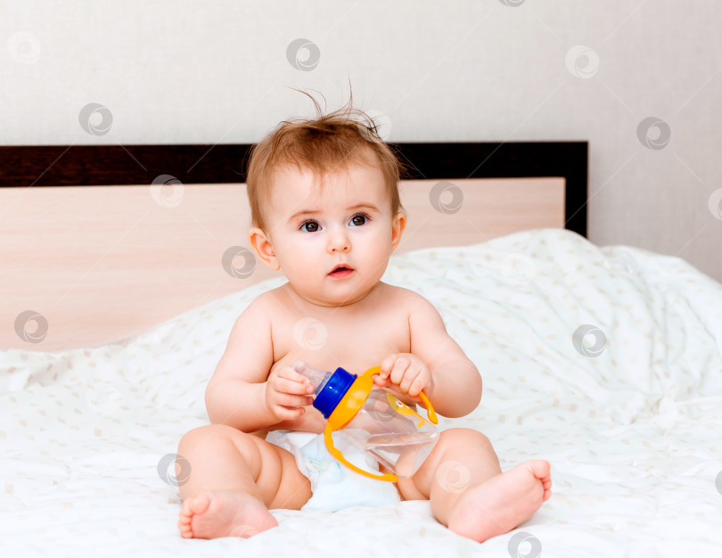 Скачать ребенок в возрасте 6 месяцев пьет воду из бутылочки, лежа на кровати. счастливый и радостный малыш фотосток Ozero