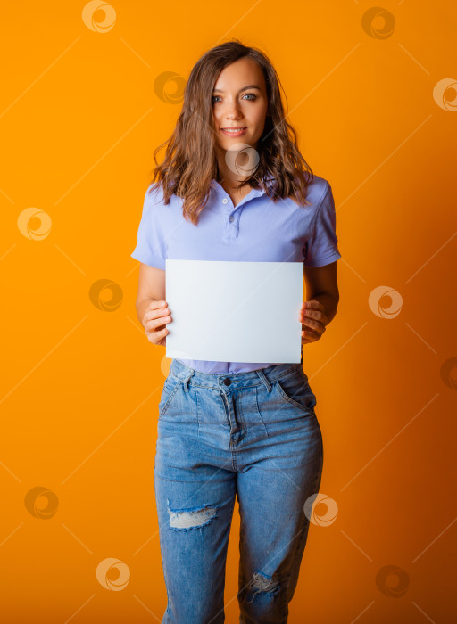 Скачать молодая красивая блондинка в голубой футболке и джинсах держит в руках белый лист бумаги. пространство для копирования. фотосток Ozero