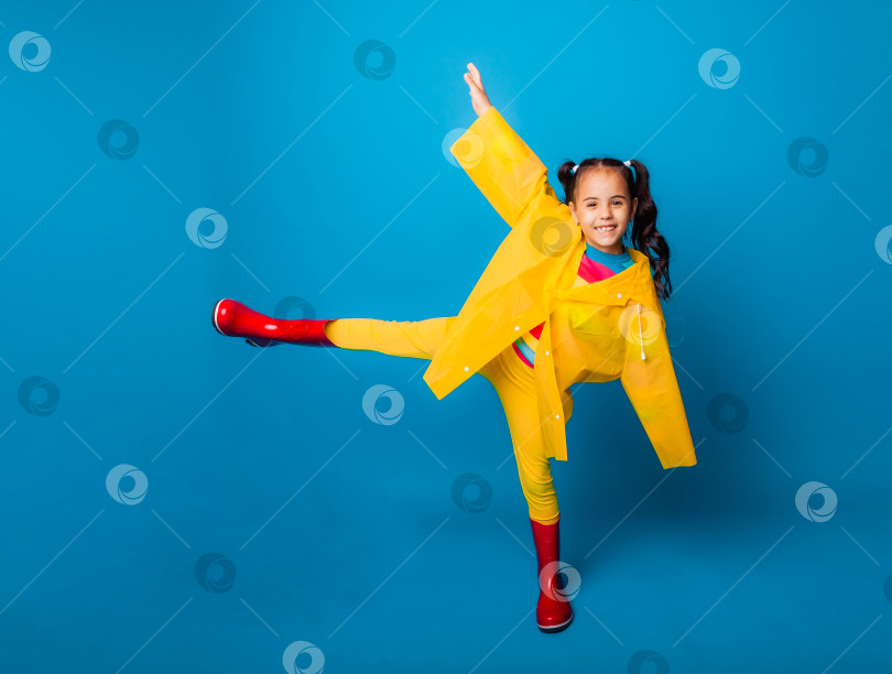 Скачать Счастливая маленькая девочка в желтом плаще и красных сапожках на синем фоне. фотосток Ozero