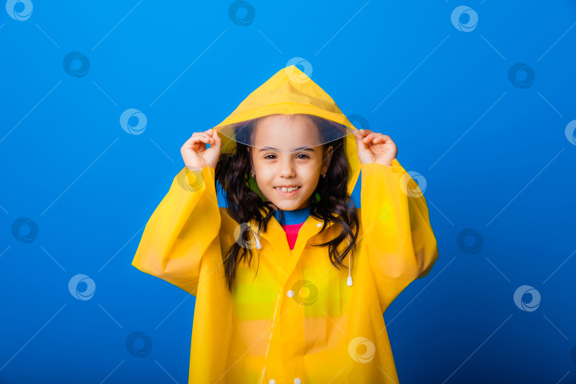 Скачать Счастливая маленькая девочка в желтом плаще и красных сапожках на синем фоне. фотосток Ozero