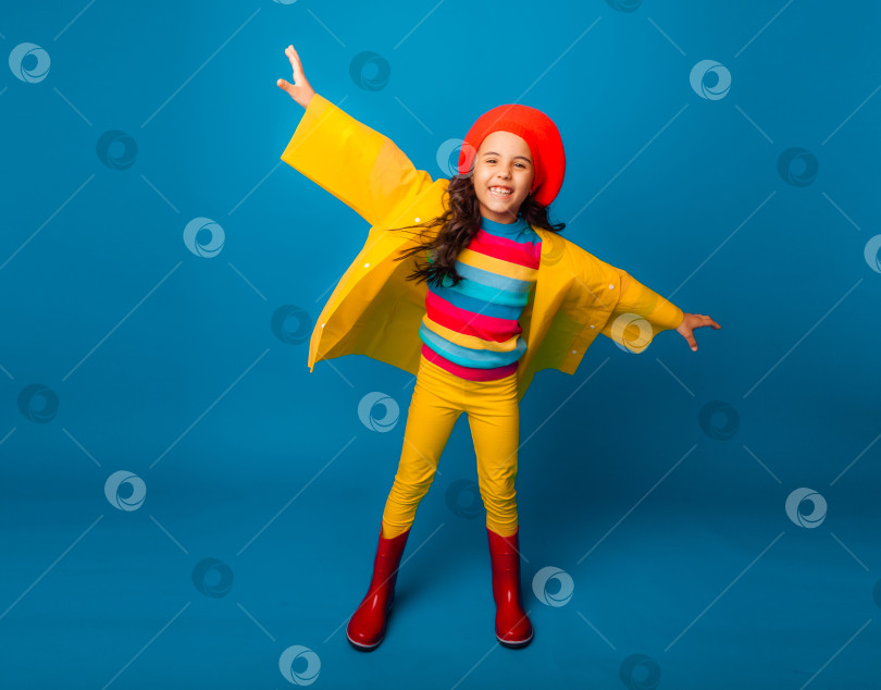 Скачать веселая девушка в желтом плаще, красном берете и резиновых сапогах прыгает с раскинутыми руками и смотрит в камеру. фотосток Ozero