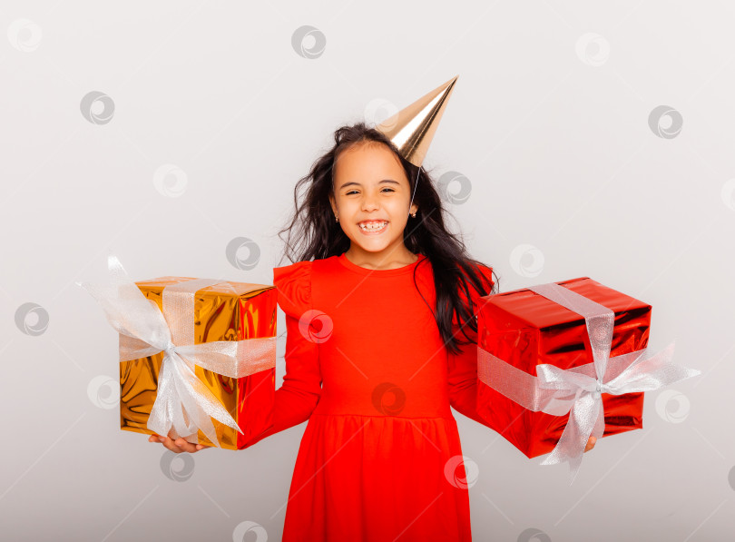 Скачать Счастливая маленькая девочка в праздничной шапочке держит в руках большую красную подарочную коробку. концепция праздника, место для текста фотосток Ozero