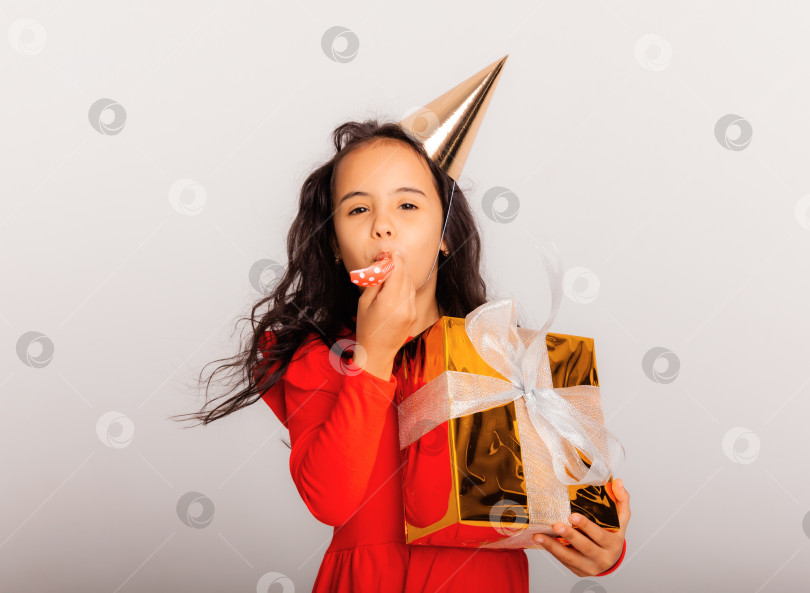 Скачать Счастливая маленькая девочка в праздничной шапочке держит в руках большую красную подарочную коробку. концепция праздника, место для текста фотосток Ozero