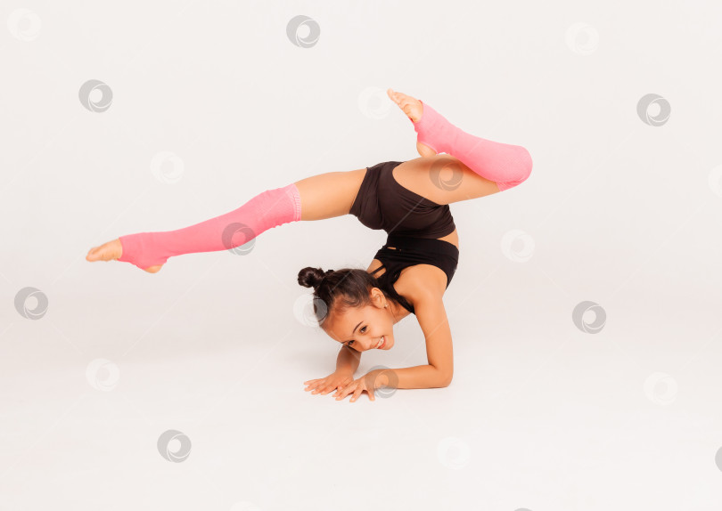 Скачать маленькая девочка-гимнастка на белом фоне. спортивные упражнения. растягивание. гибкость. аэробика фотосток Ozero