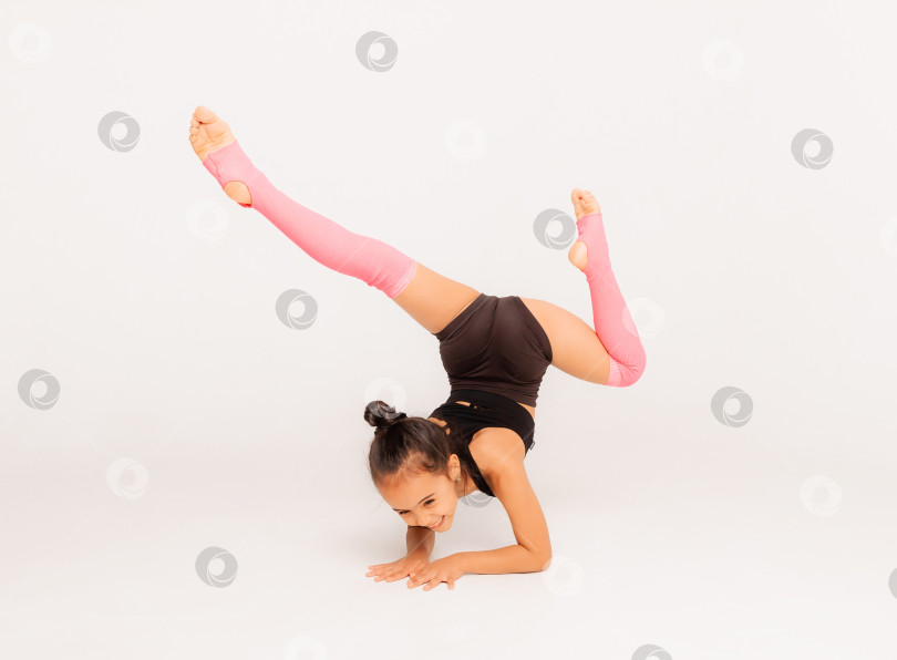 Скачать маленькая девочка-гимнастка на белом фоне. спортивные упражнения. растягивание. гибкость. аэробика фотосток Ozero