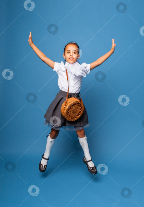 Скачать веселая школьница 7 лет с сумкой через плечо, прыгающая на синем фоне. фотосток Ozero