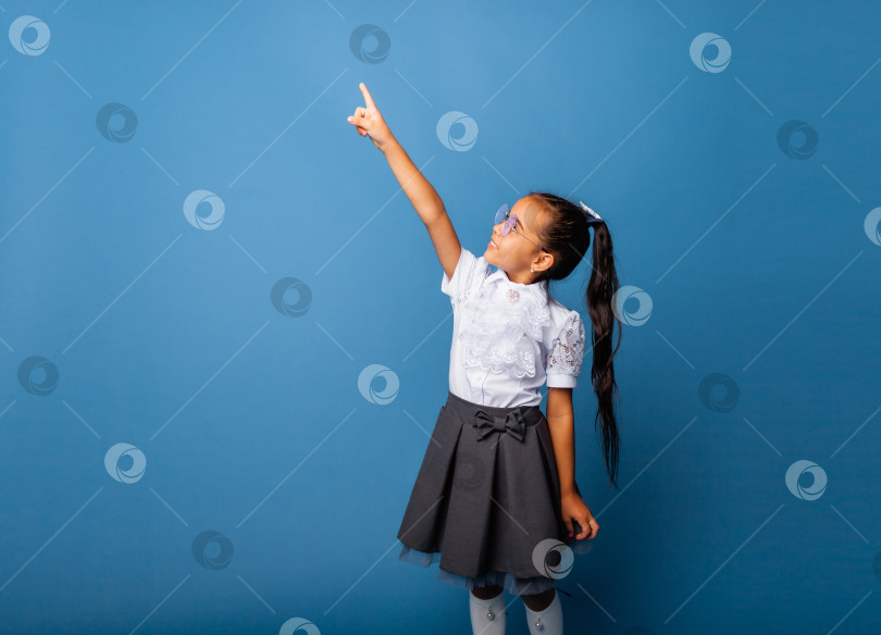 Скачать Симпатичная симпатичная жизнерадостная школьница, указывающая пальцем в сторону, копирует пространство, выделенное на синем фоне фотосток Ozero