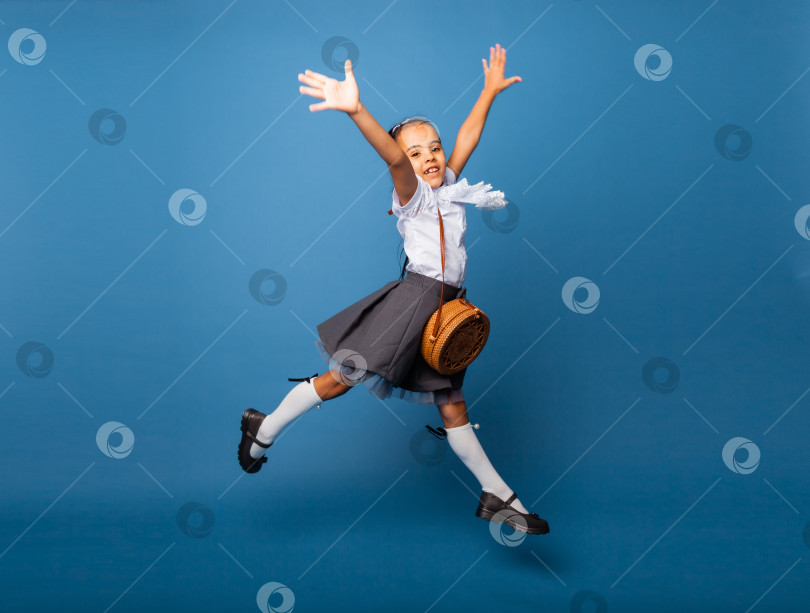 Скачать веселая школьница 7 лет с сумкой через плечо, прыгающая на синем фоне. фотосток Ozero