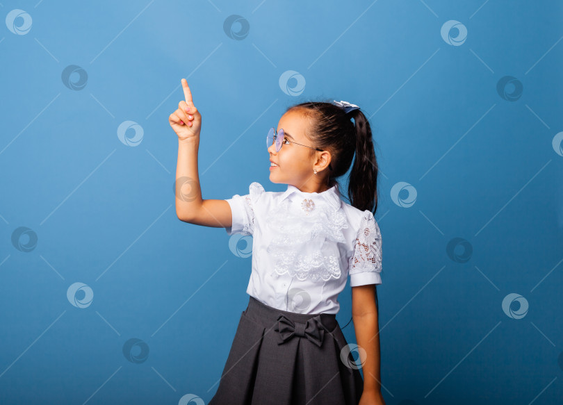 Скачать Симпатичная симпатичная жизнерадостная школьница, указывающая пальцем в сторону, копирует пространство, выделенное на синем фоне фотосток Ozero