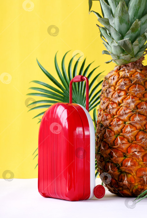 Скачать Красный чемодан и ананас на желтом фоне с пальмовыми листьями. фотосток Ozero