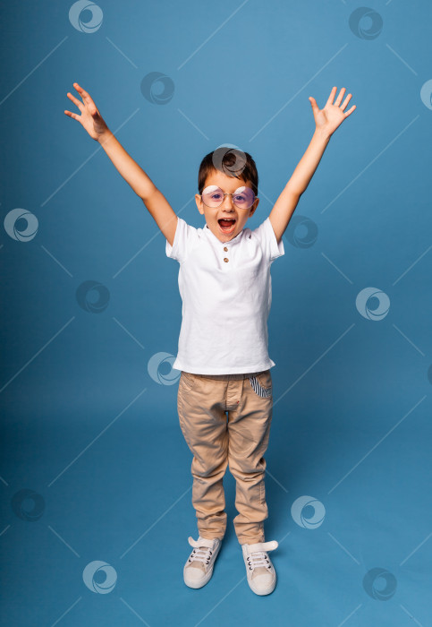 Скачать Счастливый маленький мальчик, торжествующий с поднятыми руками на синем фоне. фотосток Ozero
