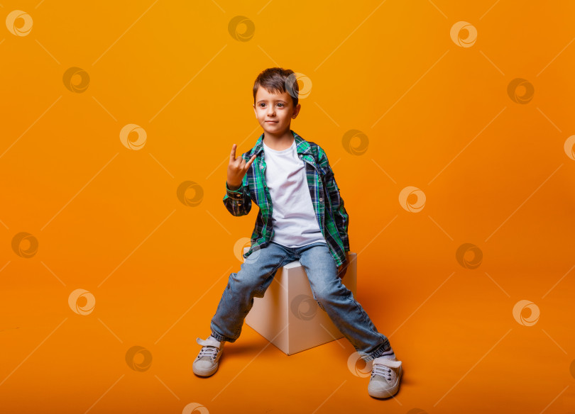 Скачать Портрет мальчика, делающего рок-жест, выделенный на желтом фоне. Красивый кавказский мальчик показывает рога жестом вверх. фотосток Ozero