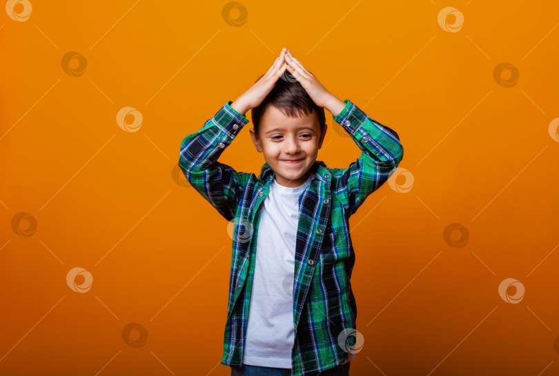 Скачать Изображение мальчика крупным планом, держащего две руки над головой и делающего жест в сторону крыши, на желтом фоне. фотосток Ozero